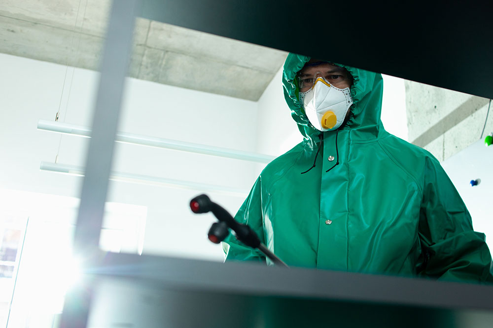 A man in green protective suit doing Fogging Spray Cleaning Services